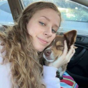 Young woman with curly hair cuddling a sleeping brown and white dog.