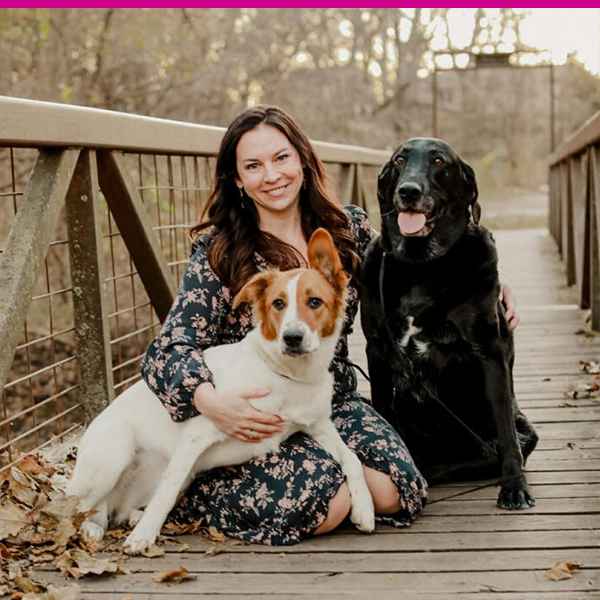 Woman seated on a bridge with a black labrador and a small white and tan dog.