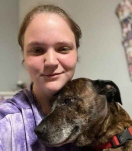Woman in a purple shirt smiling with a brown brindle dog.