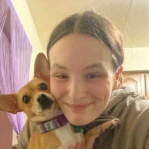 A young woman smiling with a cheerful small dog in her arms.
