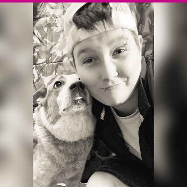 Person in a cap smiling with a dog looking up at them.
