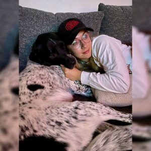 Woman in glasses cuddling with a black and white dog on a sofa.